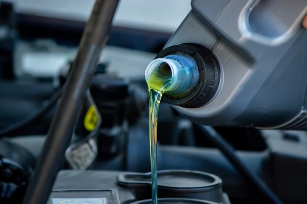 An auto mechanic changing oil pours oil into a car engine.